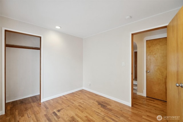 unfurnished bedroom with baseboards, recessed lighting, arched walkways, a closet, and light wood-type flooring