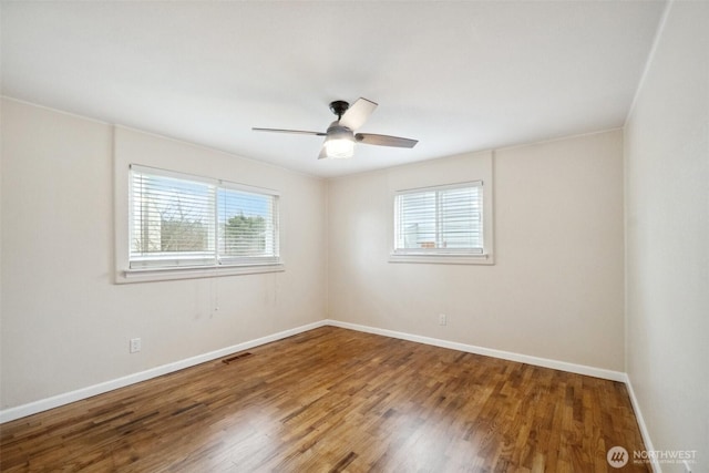 empty room with visible vents, a ceiling fan, baseboards, and wood finished floors