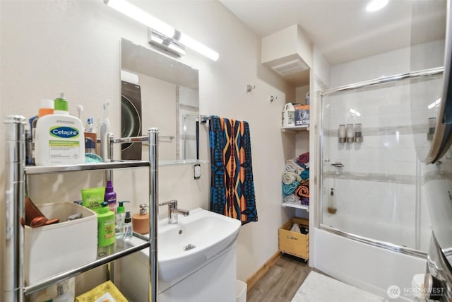 bathroom featuring combined bath / shower with glass door, washer / dryer, and wood finished floors