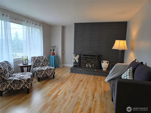 living room featuring a brick fireplace, wood finished floors, and baseboards