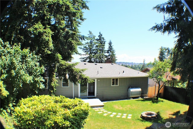 back of house featuring a chimney, an outdoor fire pit, heating fuel, fence, and a lawn