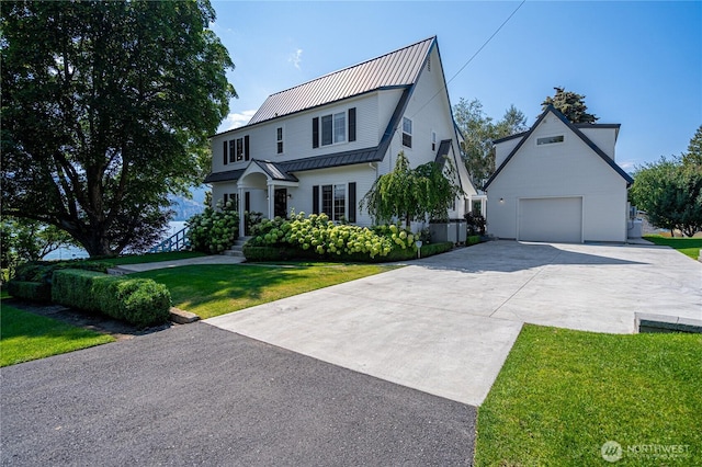 view of front of house with a front yard, concrete driveway, an outdoor structure, a detached garage, and metal roof