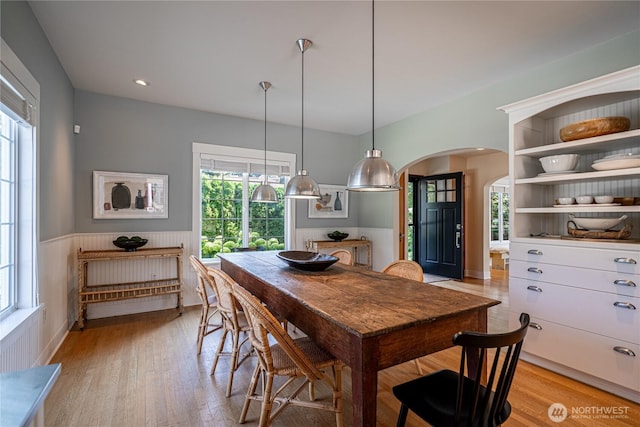 dining room featuring light wood-type flooring, arched walkways, and wainscoting