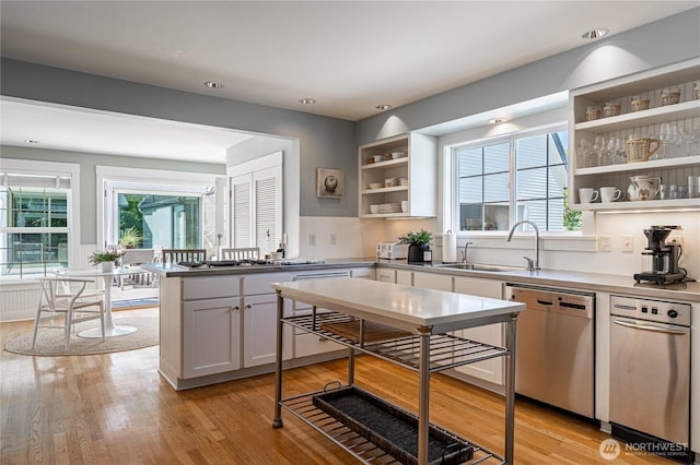 kitchen featuring stainless steel dishwasher, open shelves, light wood-style flooring, and a sink