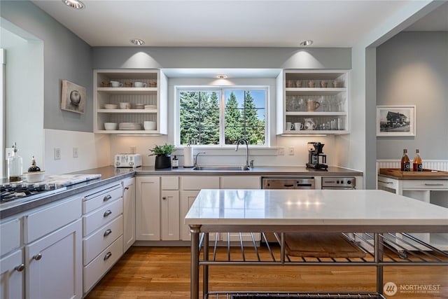 kitchen with a sink, open shelves, wood finished floors, white cabinets, and dishwasher