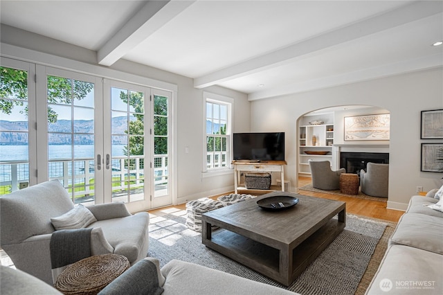 living room with baseboards, beamed ceiling, built in features, wood finished floors, and a glass covered fireplace