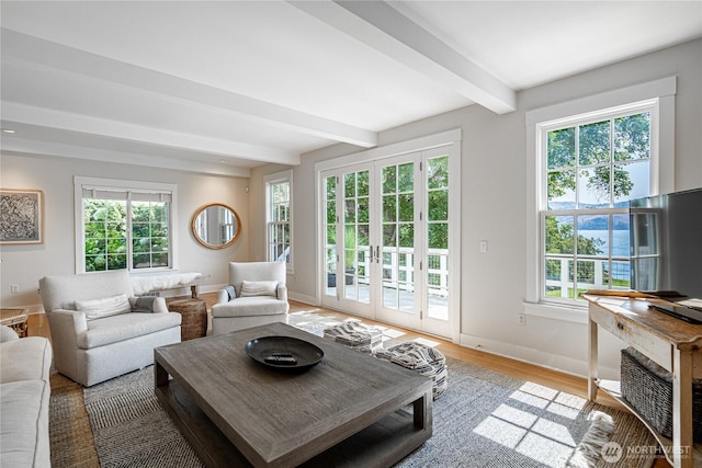 living area with beamed ceiling, baseboards, a healthy amount of sunlight, and light wood-style flooring