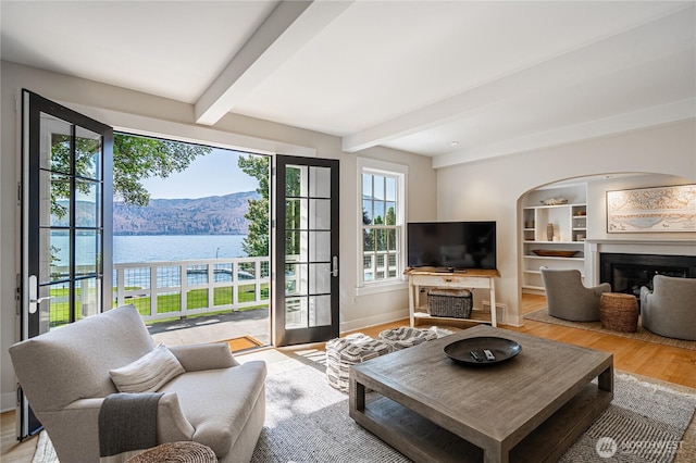 living area featuring a fireplace, beamed ceiling, wood finished floors, and baseboards