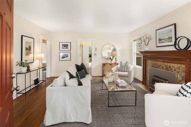 living area with dark wood finished floors, a tiled fireplace, and baseboards