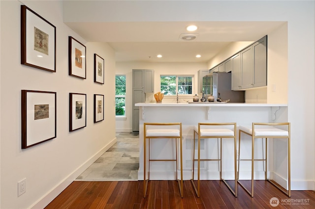 kitchen featuring gray cabinetry, a kitchen breakfast bar, light countertops, and freestanding refrigerator