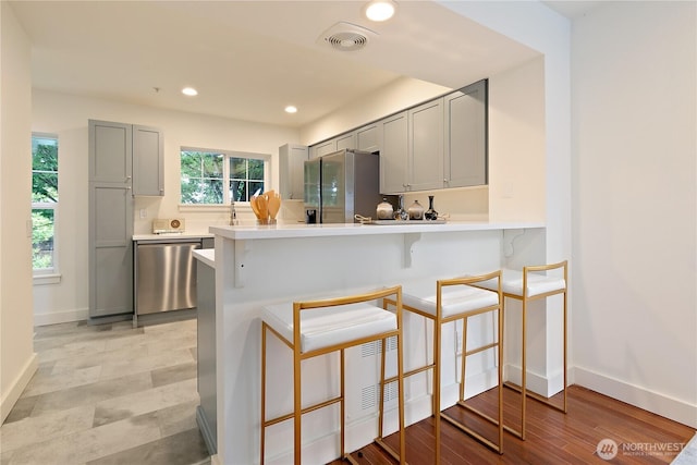 kitchen featuring stainless steel appliances, a kitchen bar, light countertops, and gray cabinetry