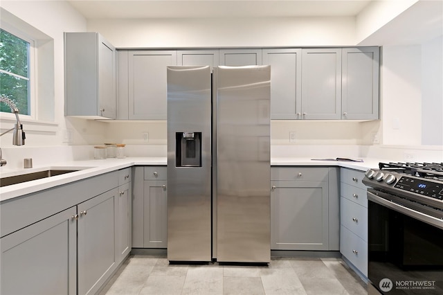 kitchen with gray cabinets, stainless steel appliances, a sink, and light countertops