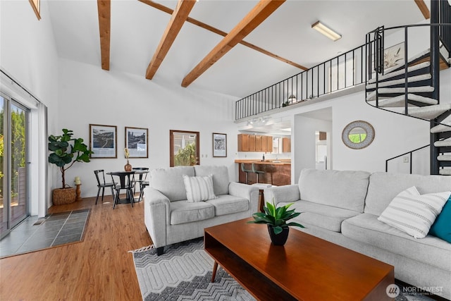 living area featuring stairway, beamed ceiling, a towering ceiling, and wood finished floors