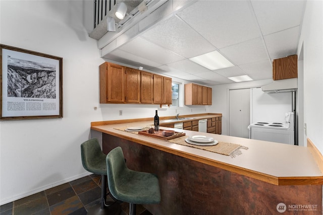 kitchen featuring under cabinet range hood, white appliances, baseboards, light countertops, and brown cabinets