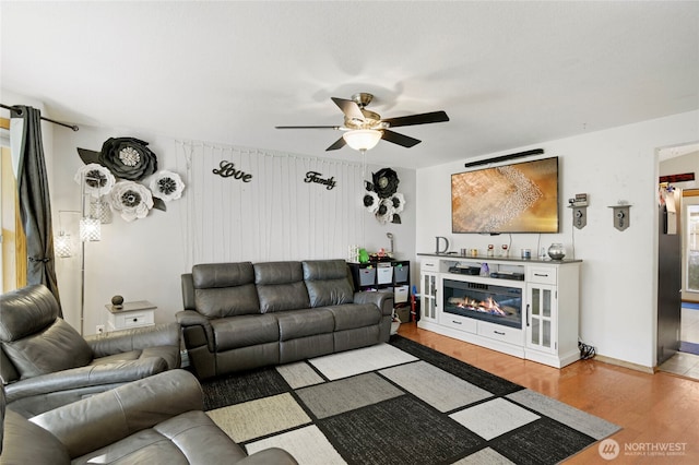 living room featuring light wood-style floors, a glass covered fireplace, and a ceiling fan