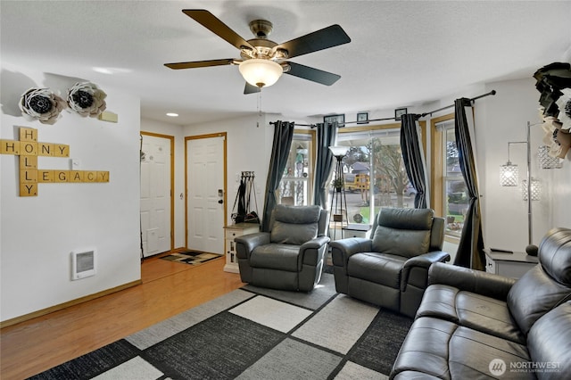 living area with ceiling fan, a textured ceiling, baseboards, and wood finished floors