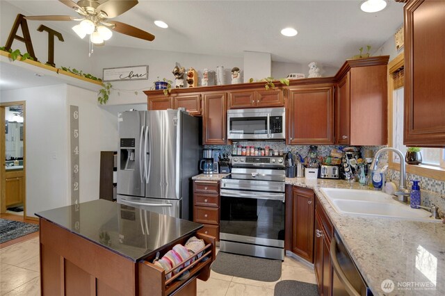 kitchen featuring decorative backsplash, lofted ceiling, appliances with stainless steel finishes, light stone countertops, and a sink