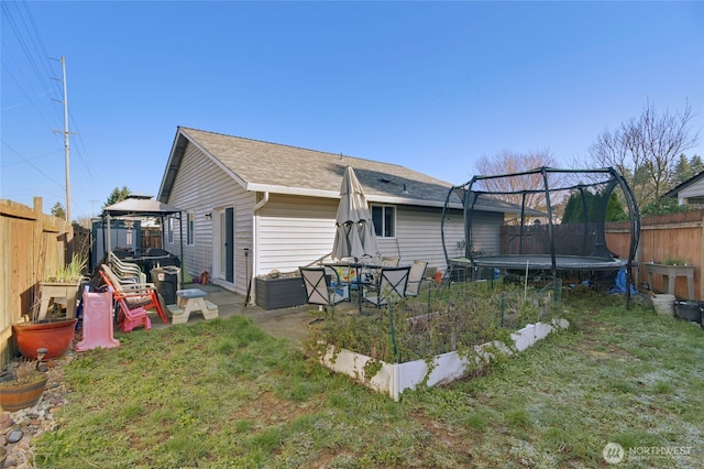 rear view of property with a trampoline, a garden, a fenced backyard, and a gazebo