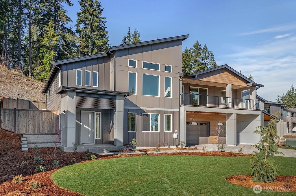 view of front facade with an attached garage, a balcony, fence, board and batten siding, and a front yard