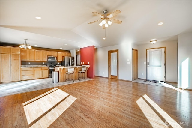 kitchen with appliances with stainless steel finishes, light countertops, light wood-type flooring, and vaulted ceiling