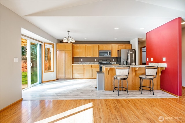 kitchen with light wood-type flooring, stainless steel appliances, a peninsula, light countertops, and a chandelier