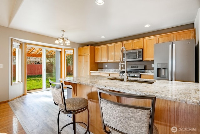 kitchen featuring light stone countertops, an inviting chandelier, recessed lighting, stainless steel appliances, and light wood-type flooring