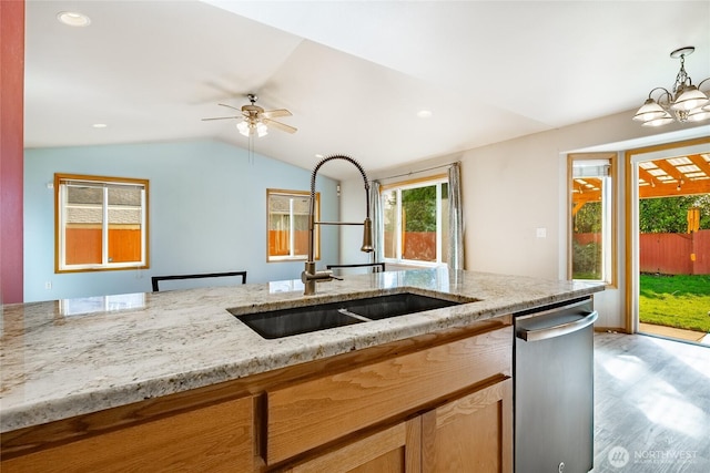 kitchen featuring stainless steel dishwasher, vaulted ceiling, light stone countertops, and a sink