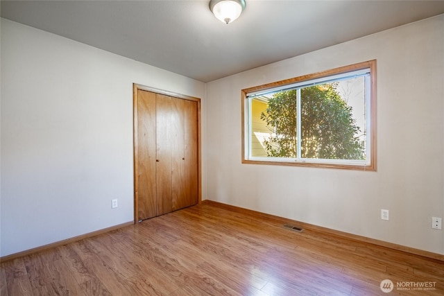 unfurnished bedroom featuring a closet, visible vents, baseboards, and wood finished floors