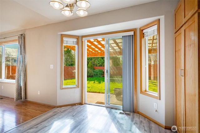 doorway to outside featuring light wood-type flooring, an inviting chandelier, a healthy amount of sunlight, and visible vents