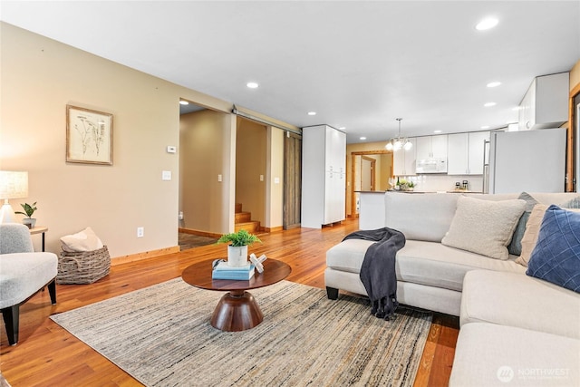 living area with recessed lighting, light wood-type flooring, a notable chandelier, and stairway