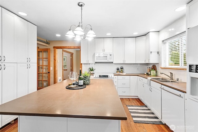 kitchen with a sink, white appliances, light wood finished floors, and white cabinetry