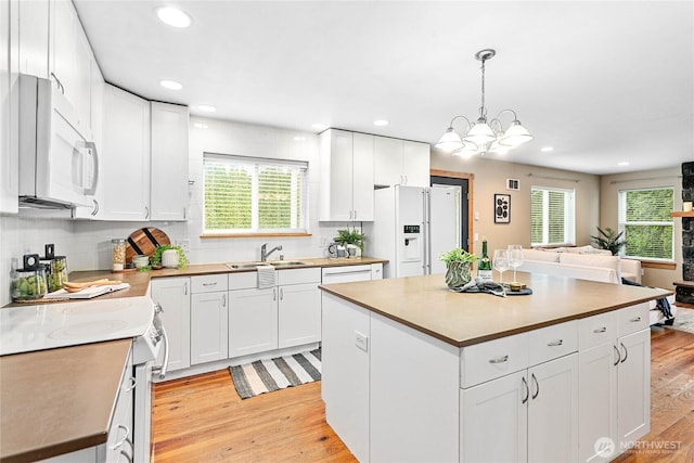 kitchen with backsplash, light wood-type flooring, white appliances, white cabinetry, and a sink