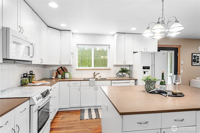 kitchen with light wood finished floors, white appliances, white cabinetry, and a sink