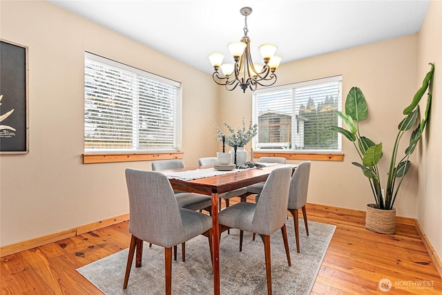 dining area featuring light wood finished floors, a notable chandelier, and baseboards