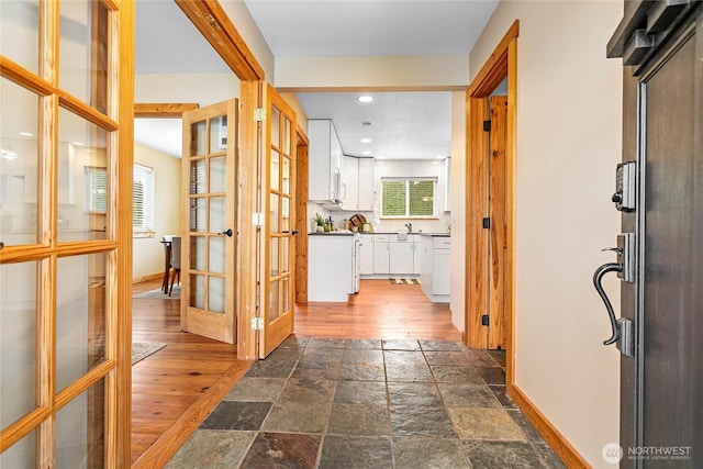 hallway featuring baseboards, recessed lighting, a sink, stone tile flooring, and french doors