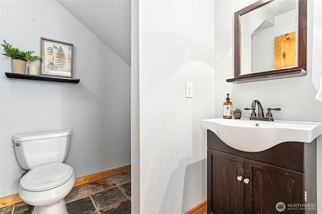 bathroom featuring vanity, stone tile floors, baseboards, lofted ceiling, and toilet