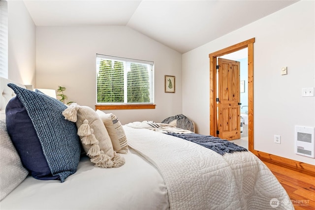 bedroom with heating unit, wood finished floors, and vaulted ceiling