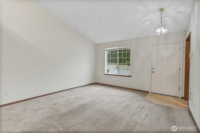 carpeted empty room featuring lofted ceiling, a notable chandelier, and baseboards