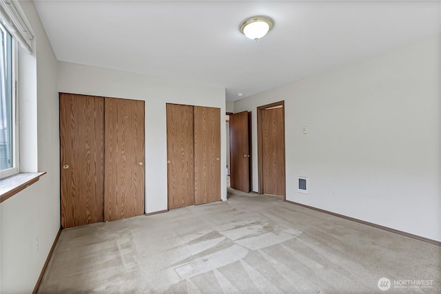 unfurnished bedroom with light carpet, baseboards, visible vents, and multiple closets