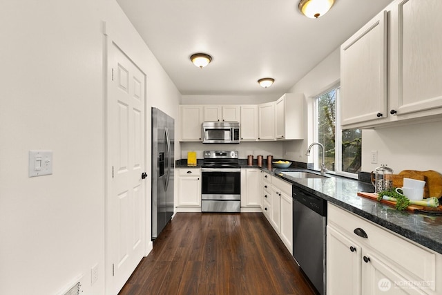 kitchen featuring dark wood-style floors, appliances with stainless steel finishes, white cabinets, and a sink