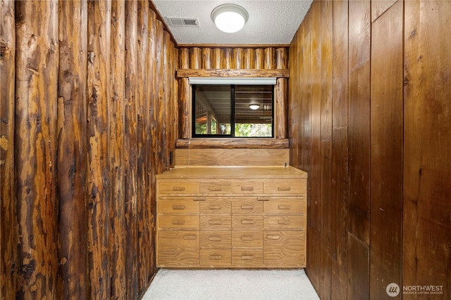 interior space with carpet, visible vents, wood walls, and a textured ceiling