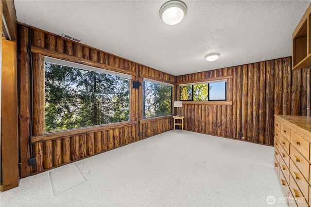 empty room featuring wooden walls, visible vents, and a textured ceiling