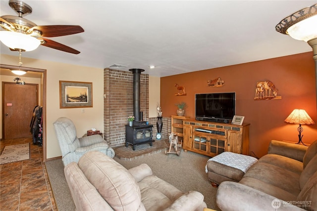 living room featuring a wood stove, ceiling fan, visible vents, and carpet flooring