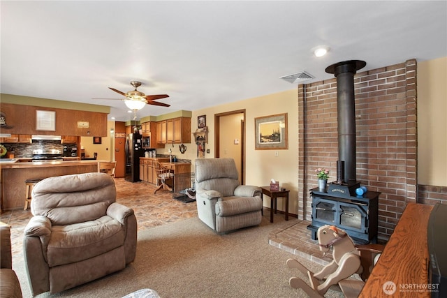 living room with light colored carpet, a wood stove, visible vents, and ceiling fan