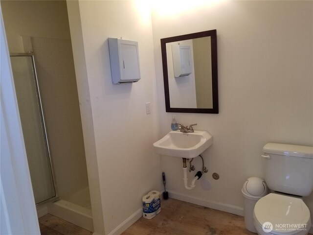 bathroom featuring toilet, baseboards, a stall shower, and a sink