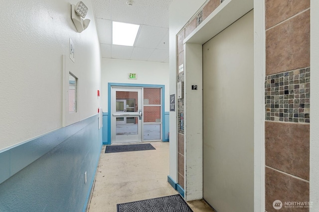 corridor featuring a drop ceiling, elevator, and concrete flooring