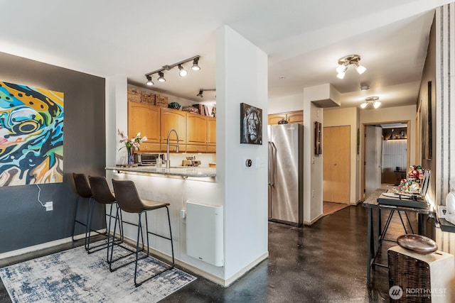 kitchen featuring baseboards, freestanding refrigerator, a sink, finished concrete floors, and a kitchen bar