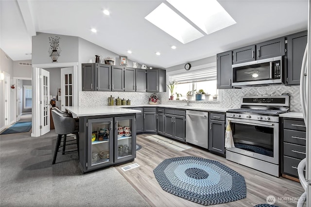 kitchen with lofted ceiling with skylight, appliances with stainless steel finishes, gray cabinets, light countertops, and backsplash