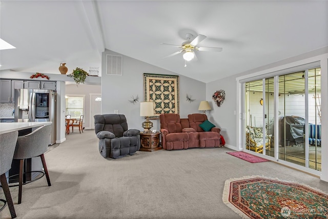 living area featuring light colored carpet, vaulted ceiling with skylight, visible vents, and a ceiling fan