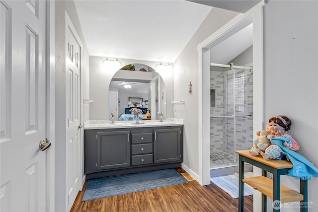 ensuite bathroom with connected bathroom, wood finished floors, a sink, double vanity, and a stall shower